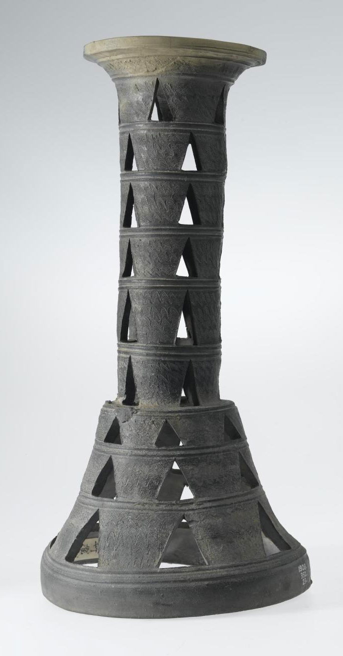 Pedestal of dark stone ware, sepulchral or ceremonial type, with comb decoration, and triangular perforations in nine stages: Japan, Chikuzen Province, Dolmen period.