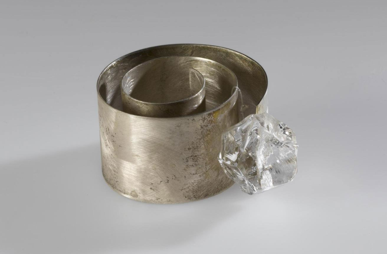 Finger-ring entitled Chikyūjō no hyōga ga tokenai yō ni inotte (Praying the Glaciers on Earth Won't Melt), made of a loosely coiled band of broad, flat silver with an irregularly-cut piece of clear glass: Japan, Osaka, by Mitsushima Kazuko, 1997. On display in the Inspired by Nature gallery at the National Museum of Scotland.