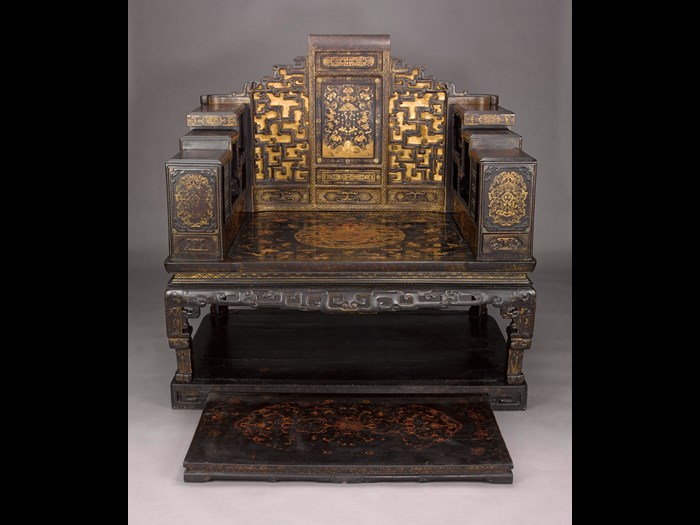 Imperial seat of black and brown lacquered wood, decorated in gold with landscapes, flowers and bats.  In the centre of the seat there is a circular medallion encompassing a five-clawed dragon among clouds; in the centre of the back there is qing (a stone music instrument) surrounded by peonies and five bats.  Finally, there is a shelf for small treasures (duobaoge) on each side and an extending foot rest: China, Qing Dynasty, 18th century AD. 