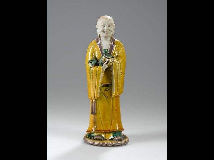 Figure of a luohan or Arhat, holding a lion cub in his arms in porcelain with sancai (three coloured) glazes, possibly Xiaoshi Luohan (Luohan with laughing Lion): China, Ming or Qing Dynasty, 16th - 18th century AD. 