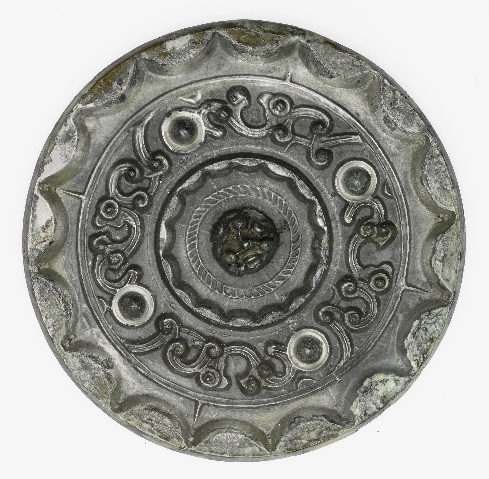 Mirror of silvered patinated bronze, with a central perforated boss in the form of a many-peaked mountain on the reverse: China, attributed to Tang dynasty, 618 - 907 AD.