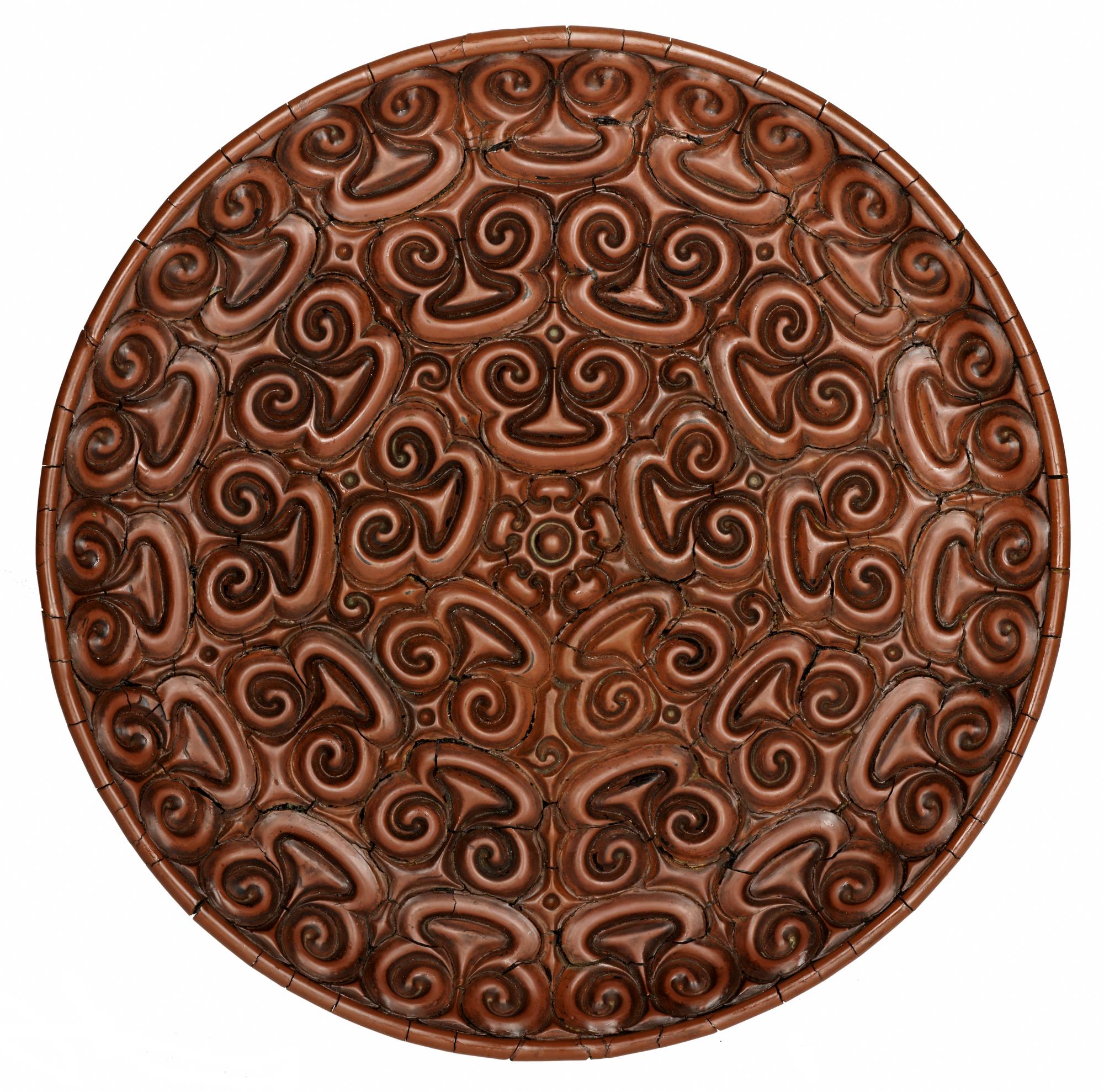 Circular dish of red lacquered wood carved on upper surface with three bands of spectacle-shaped designs surrounding a centre of petals and arrowhead patterns: China, Yuan dynasty, 14th century.