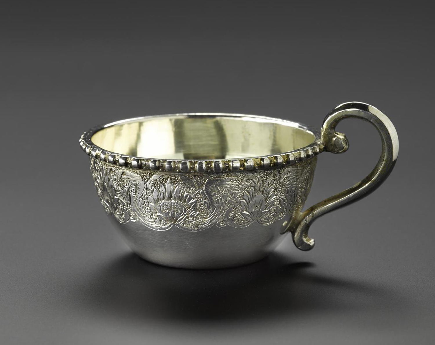 Miniature tea cup holder made of silver, with a handle at one side and floral decoration around the outside, part of a set with a saucer and a spoon, hallmarked on the bottom, Iran, probably Isfahan, 1920s-1940s, acc. no V.2015.68.1