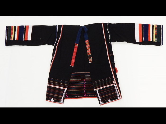 Woman's jacket of black cotton decorated with stripes in red, white, blue and yellow applique, ornamented with buttons, tin studs, cowrie shells, coins, and monkey fur tufts: Asia, South East Asia, North Thailand, Chiangrai, Hweisan or Amphur Mackon, Akha people, by Angoe, 1984.