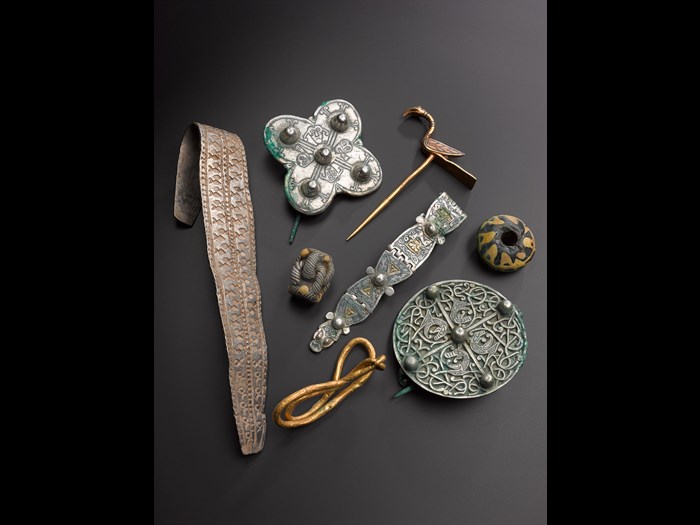 Various objects from the Galloway Hoard on a dark surface, including a gold bird pin, silver brooch and flattened silver arm-ring.
