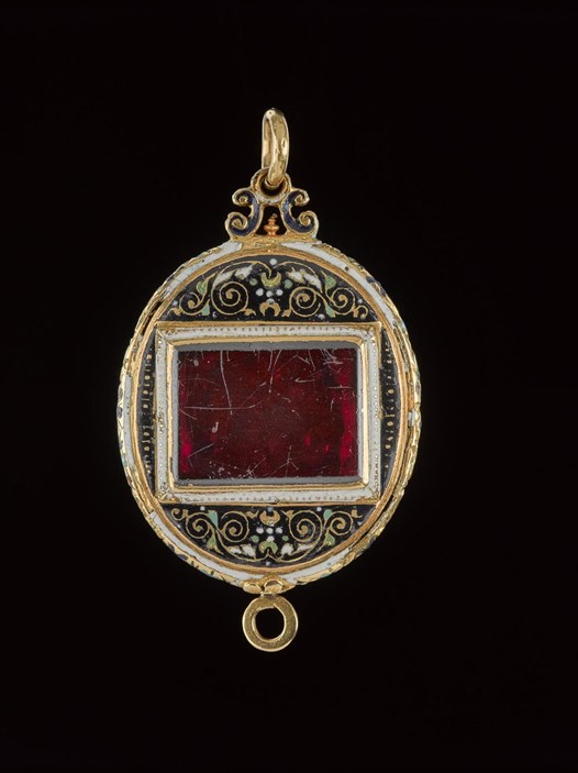 Golden jewel on a black background. A red, slightly cracked rectangular gemstone in the middle with swirling patterns around it.