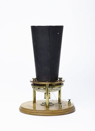 Circular wooden platform supporting a tall, black, upward-facing cone-shaped device with two wires attached at the bottom.