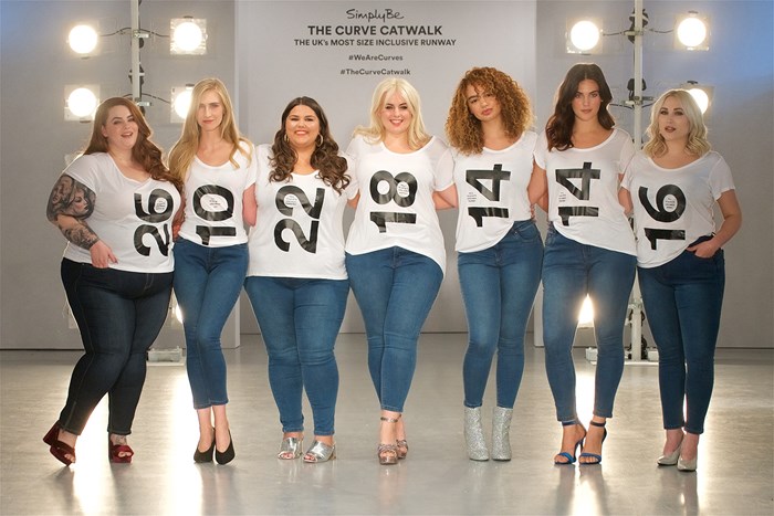 7 female models standing in a line wearing white t-shirt showing their dress sizes, ranging from 10 to 26