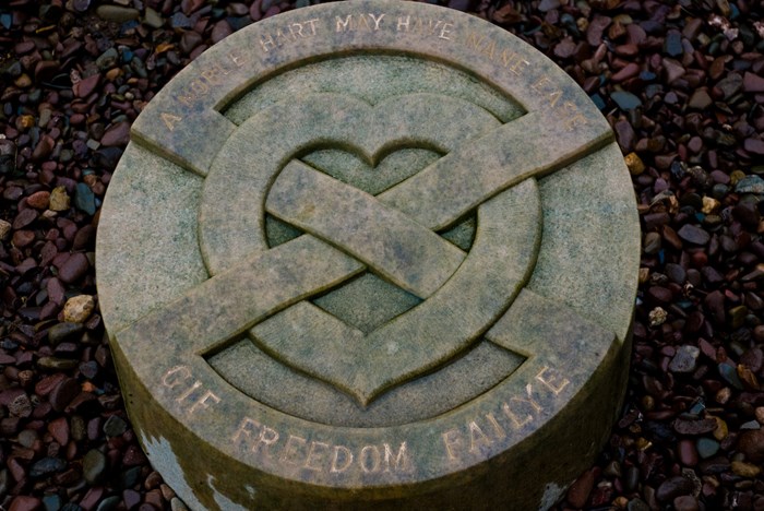 Circular stone marker for Robert Bruce's heart with a saltire and heart design in a patch of pebbles.