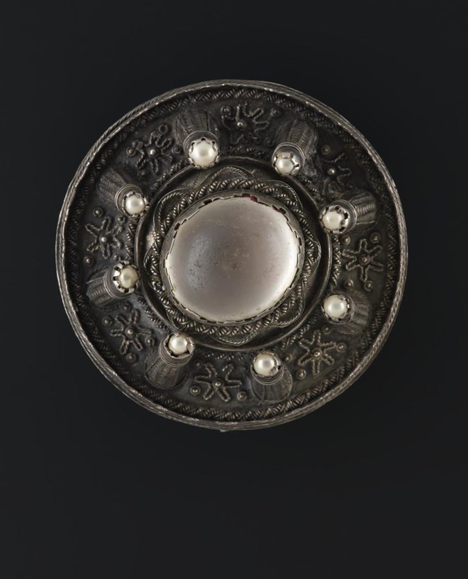 Circular brooch, dark brown or grey, with eight small pearls surrounding a central white sphere.