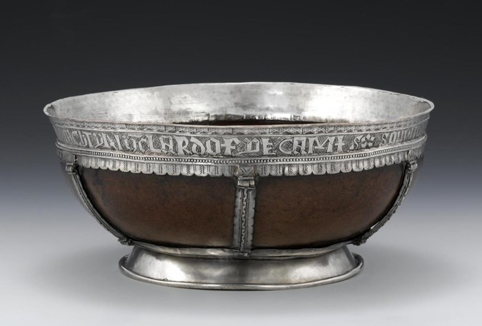 Wide and low brown metal-rimmed bowl or mazier, with script around the rim on a grey background.