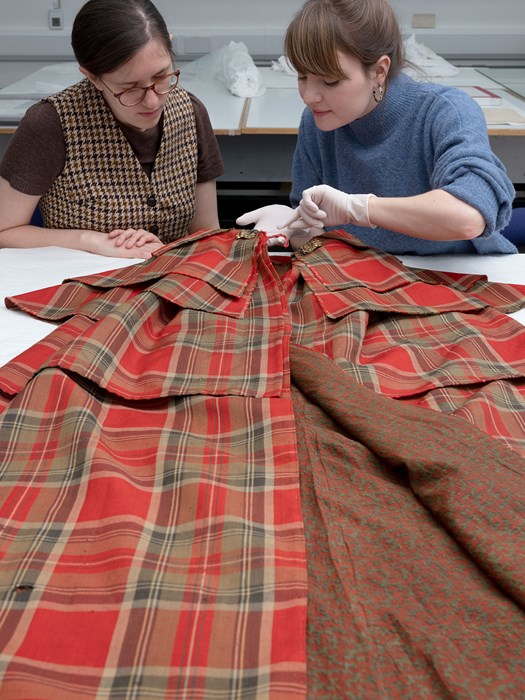 William Grant Foundation Research Fellow Rosie Waine and Baillie Gifford Textile Conservator Rosie Nuttall examine a tartan cloak.