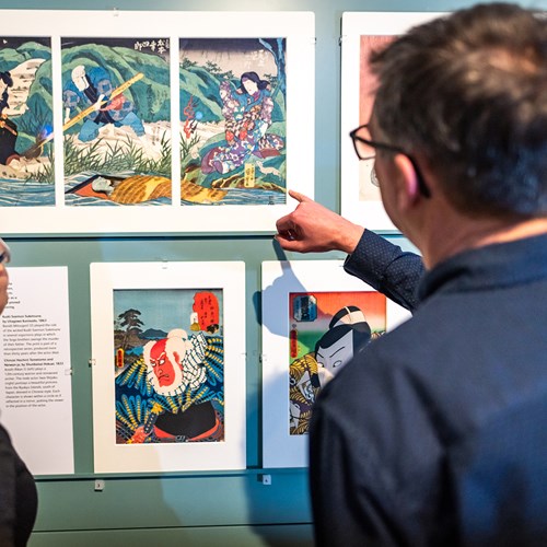 Two visitors looking at a series of Japanese prints on a wall. 