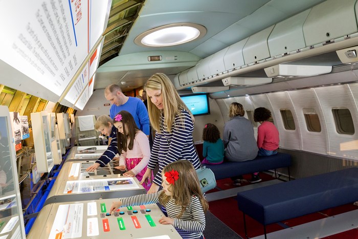 Children and adults interacting with a display inside of an aeroplane.