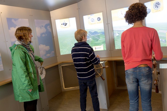 An adult and two children interacting with a flight simulator game