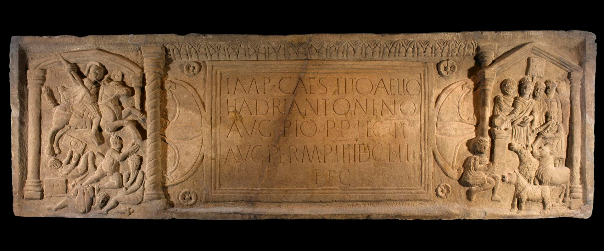 Long, off-yellow stone distance slab with Latin script in the centre and sculptured Roman figures at each end.