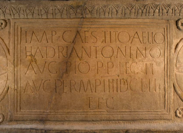 Close-up of the Latin text on the sandstone distance slab. Text covers 5 lines, including the names 'Hadrian' and 'Antonino'