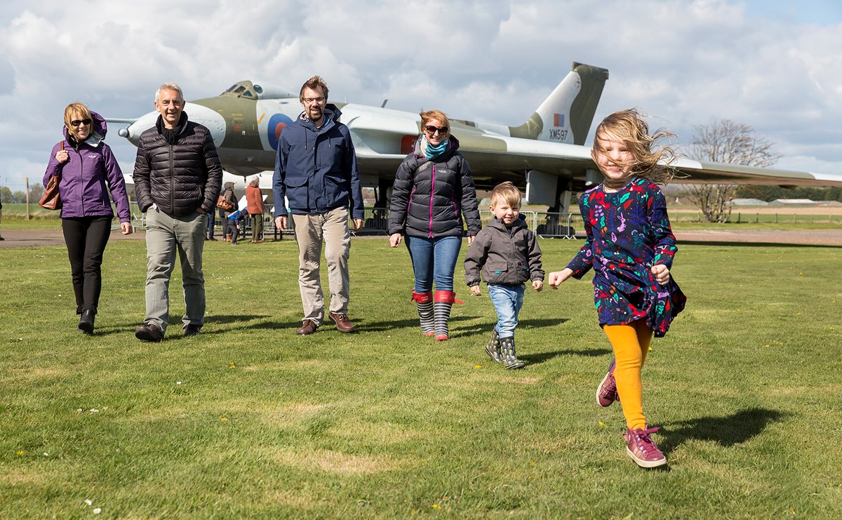 A multigenerational family walks on the grass in front of an airplane