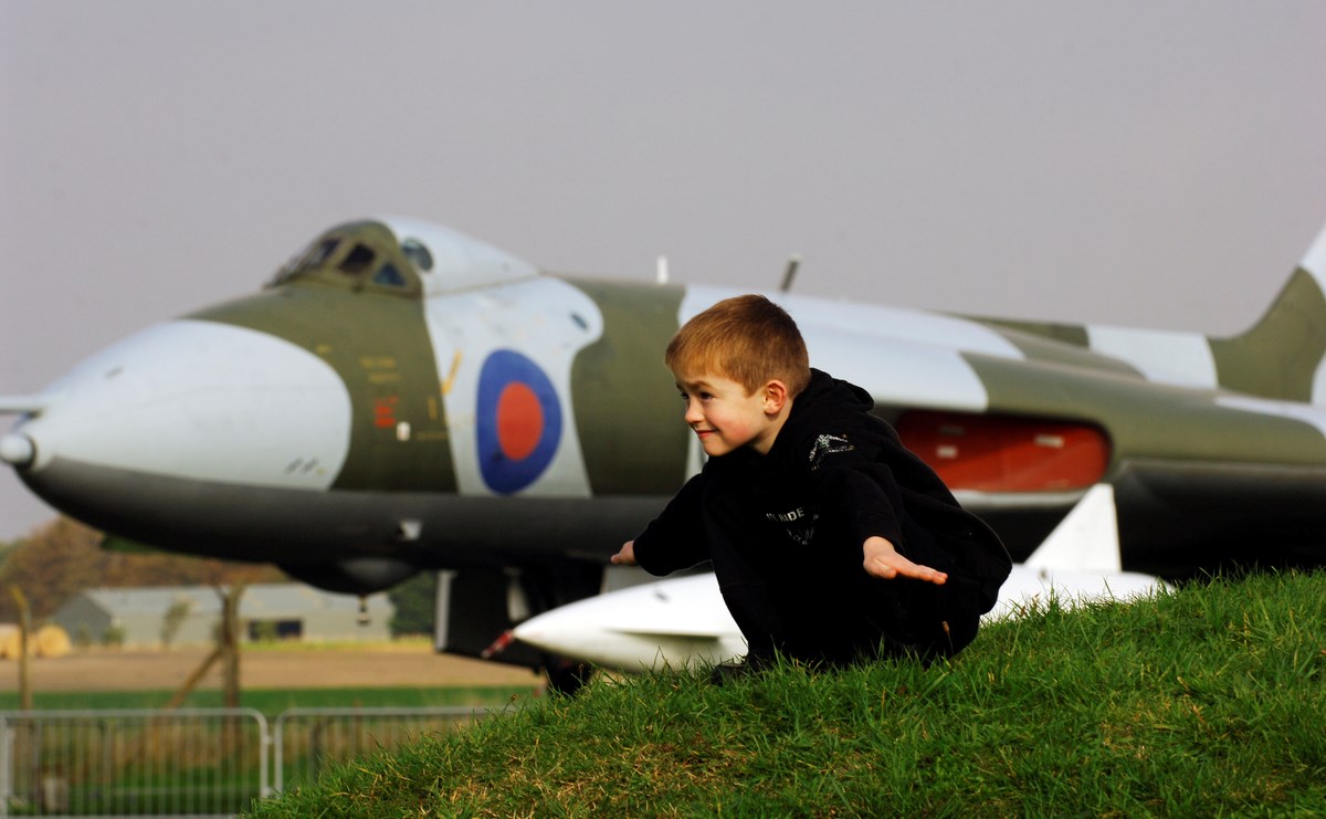 Child in holding arms out like a plane with Vulcan airplane in the background