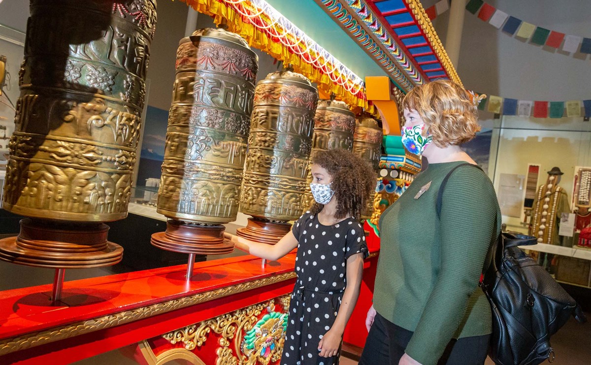 A girl spins Tibetan prayer wheels while a woman looks on behind her.