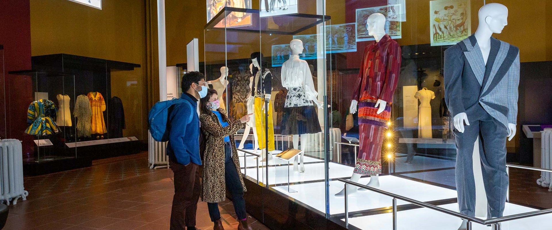 Two visitors wearing masks look at mannequins in glass cases in the Fashion and Style gallery