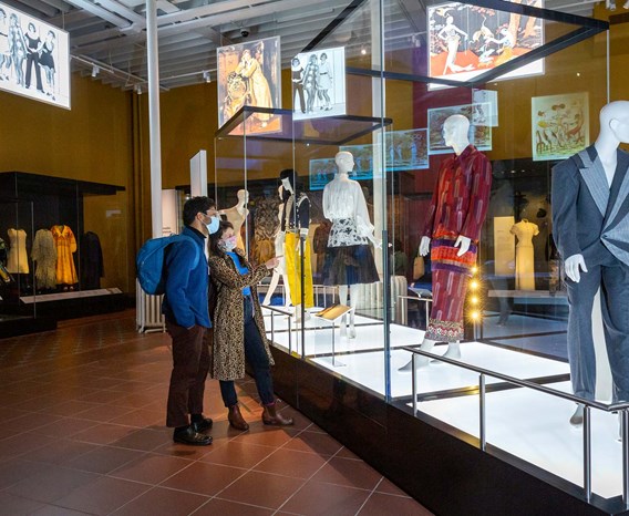 Two visitors wearing masks look at mannequins in glass cases in the Fashion and Style gallery