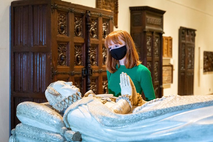 Woman in green shirt with red hair and face mask stands beside the replica tomb of Mary, Queen of Scots in the Scottish History galleries.