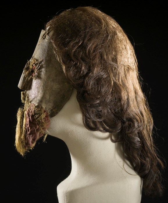 Mannequin head fitted with Peden's mask viewed in profile facing left. Brown locks of hair flow down the back.