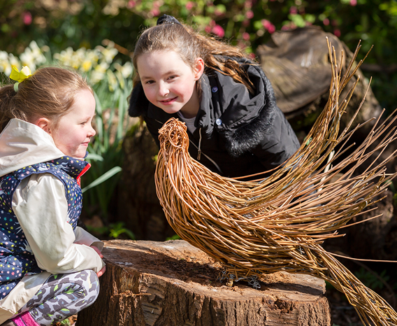 Two children looking at a willow sculpture of a pheasant.