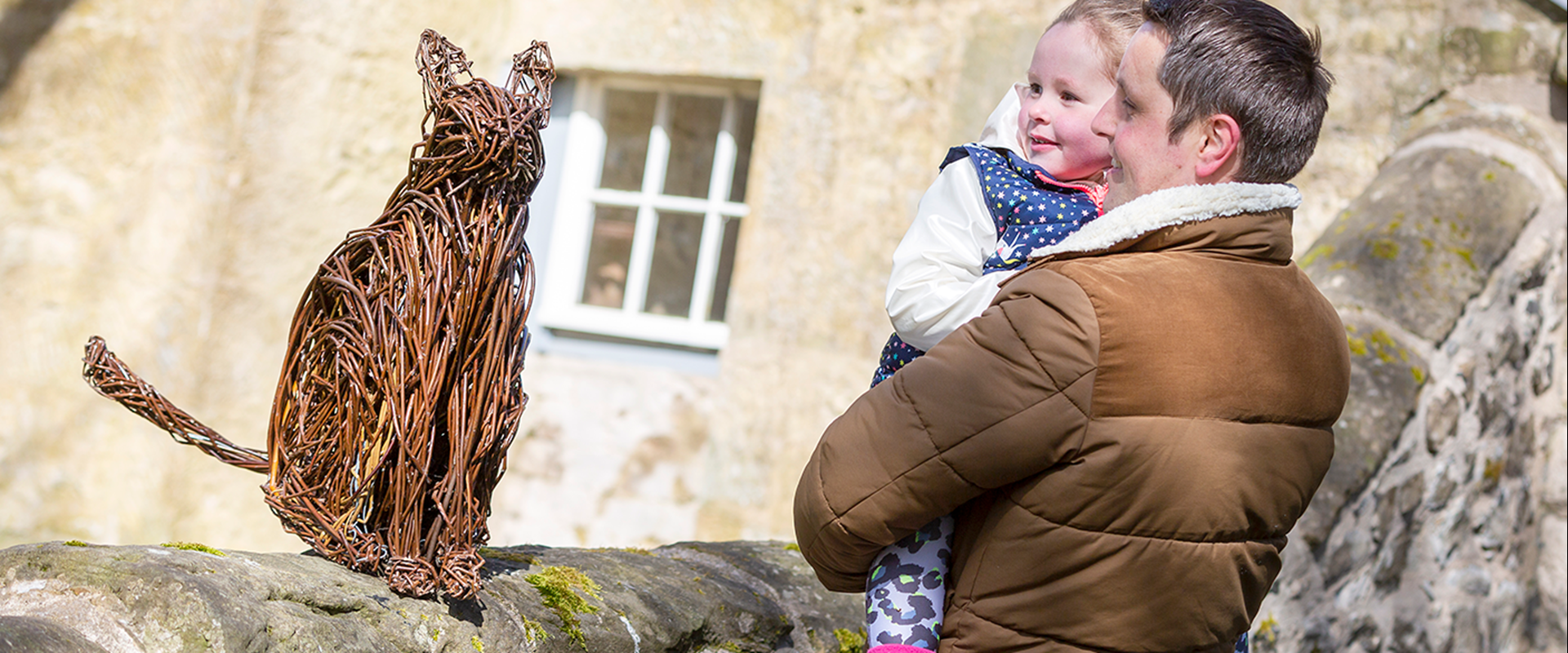 Visitors look at a willow sculpture of a cat sitting on a wall