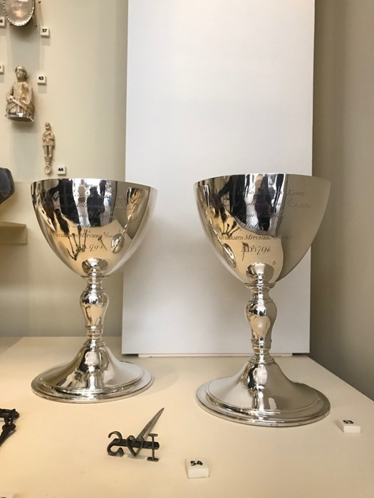 A pair of silver communion cups sitting in a museum display case.
