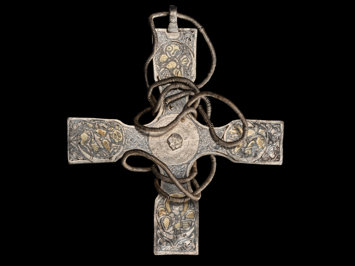 Silver cross with gold and niello designs at each terminus against a black background. A chord is wrapped around it.