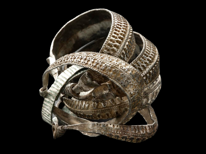 A bundle of four arm-rings form a coil-like shape. Two carved animal faces are visible, and all the rings have intricate, geometric carvings