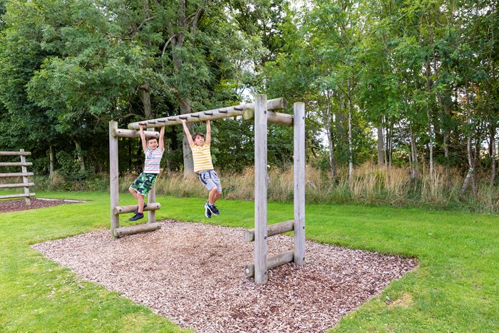 Two children swinging from a climbing frame on an assault course.