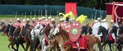Reenactors form a line of Roman cavalry on a grassy field, armed with spears, oval-shaped shields, shining helms and full-body armour.
