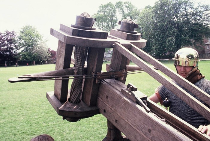 A re-enactor prepares a large ballista to fire in a green field
