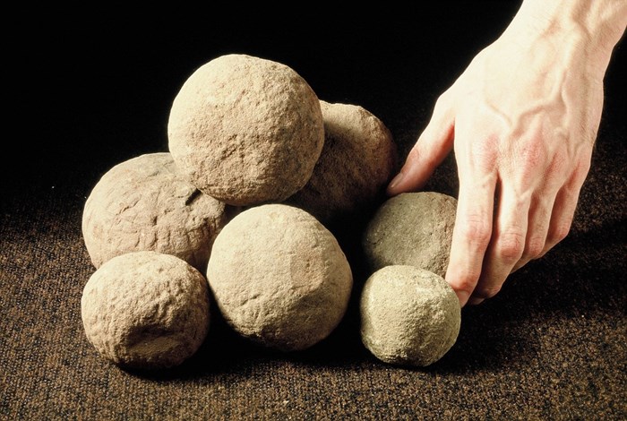 Large stone balls against a black background with a hand for scale. The balls are the size of a clenched fist.