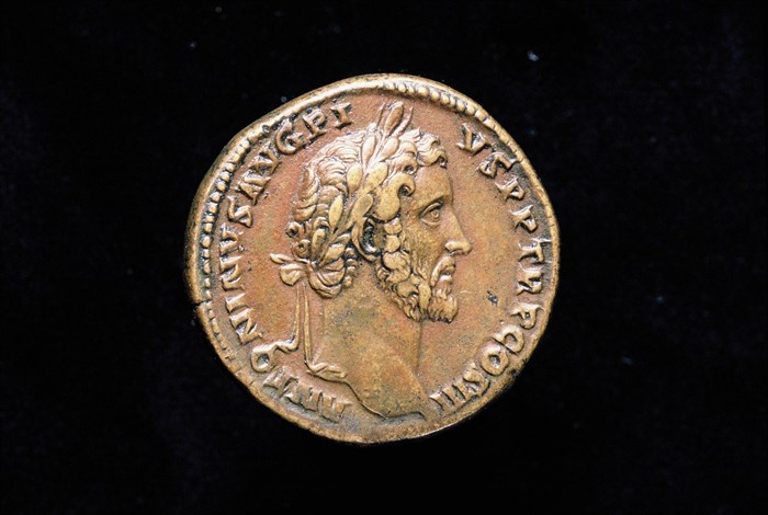 Yellow-brown coloured coin with a bearded Antoninus Pius in profile