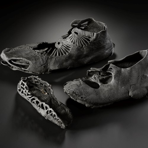 Three shoes on a black background. One is large with a radial pattern of straps, one is medium with less complex straps, and one is small with just the sole surviving.