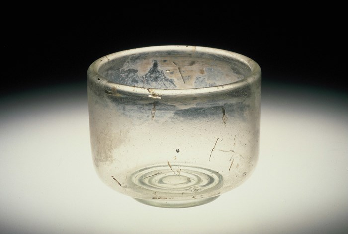 Small, wide, translucent glass cup with several scratch marks and a spiral shape at the bottom