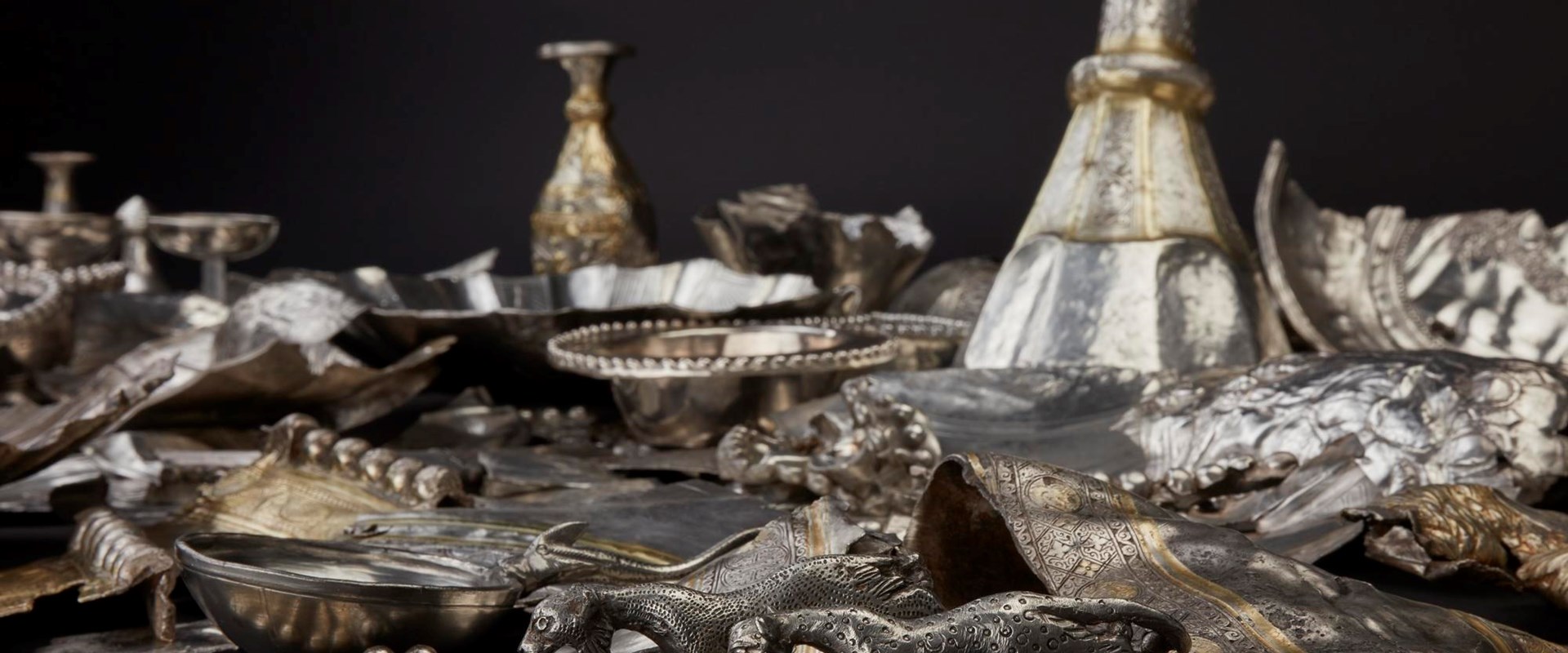 Mass of hacked silver objects including plates, cups, and two speckled figurines of panthers or lionesses.