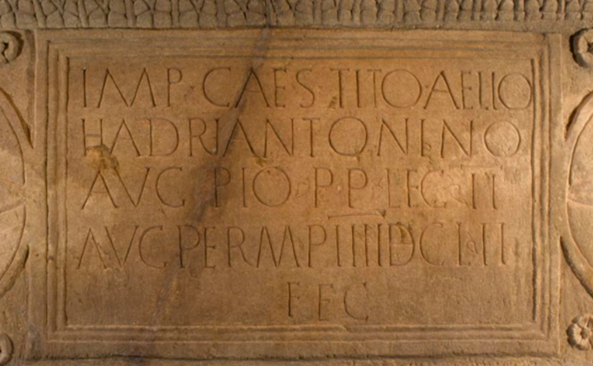 Close-up of an orange stone slab with Latin text written in neat rows across its whole surface.