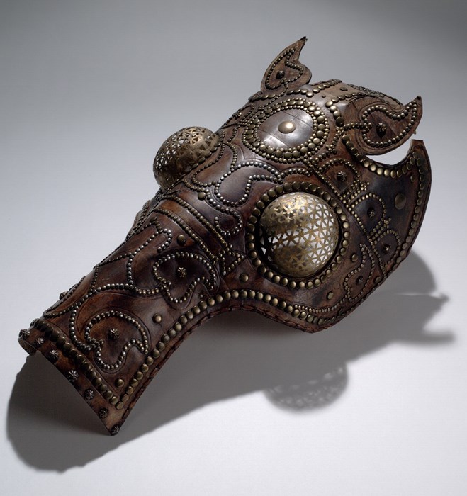 Brown leather helmet made to fit a horse's head, with bronze studs and elaborate bronze eye guards resembling fly's eyes
