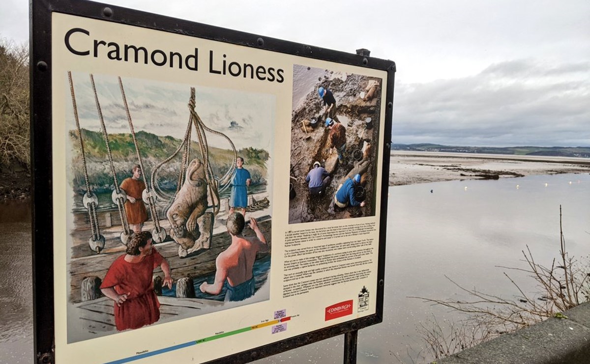 Cream-coloured sign framed in black next to a river's mouth, with a drawing of the lioness statue being deposited in the river on board a boat.