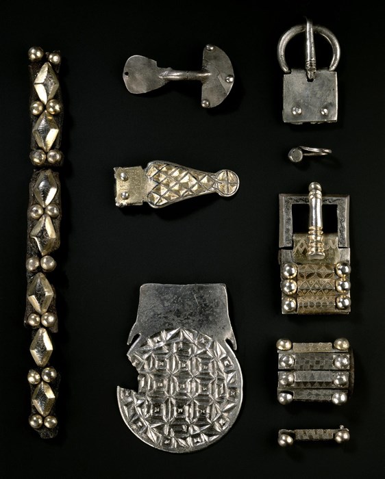 Six distinct silver objects. On left, a necklace-like ornament; in middle, three brooch clasps with diamond patterns; on right, two buckles