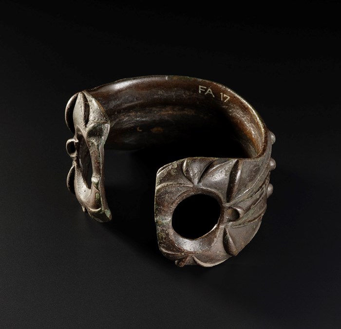 Brown armlet viewed from the front, with the opening facing forward. Two holes flank the opening and leaf-like designs cover it