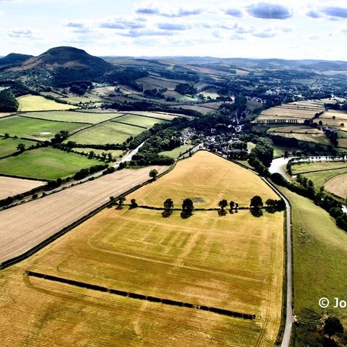 Scenic aerial image of the River Tweed and Eildon Hills on a sunny day, with crop marks from the Roman fort visible in the foreground.