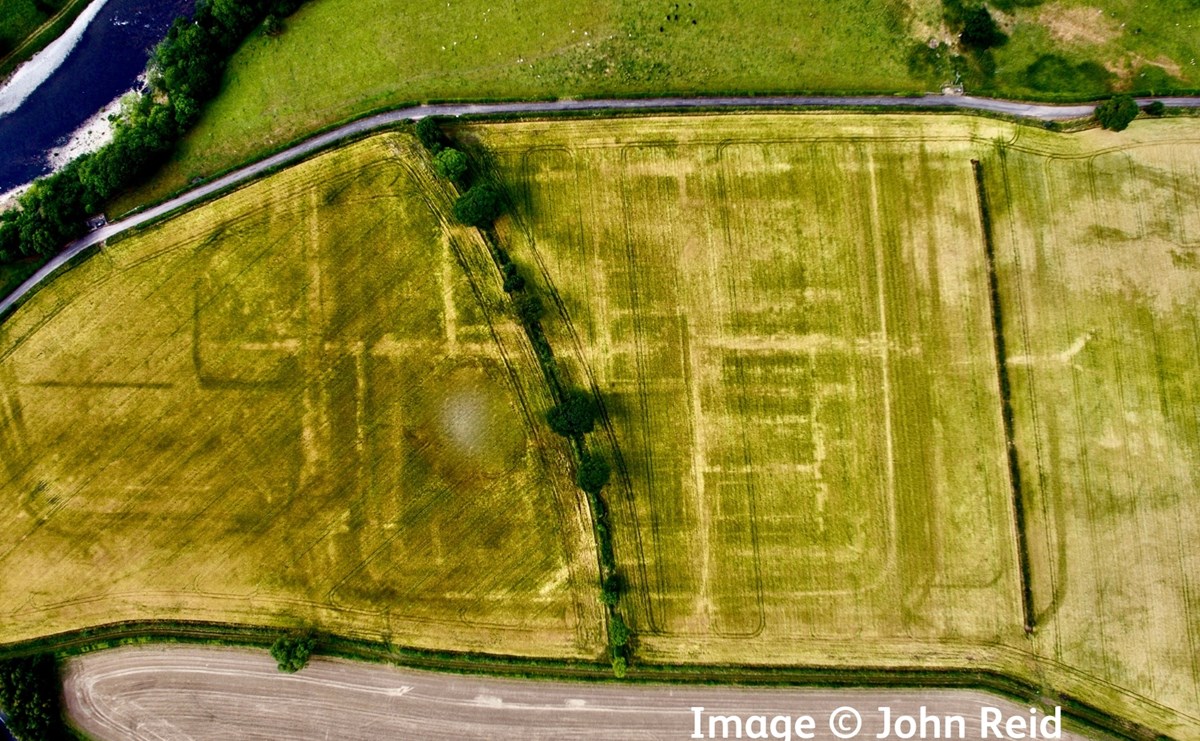 Aerial bird's eye view looking straight down on a green-yellow field, in which you can clearly see geometric lines tracing a now vanished Roman fort.