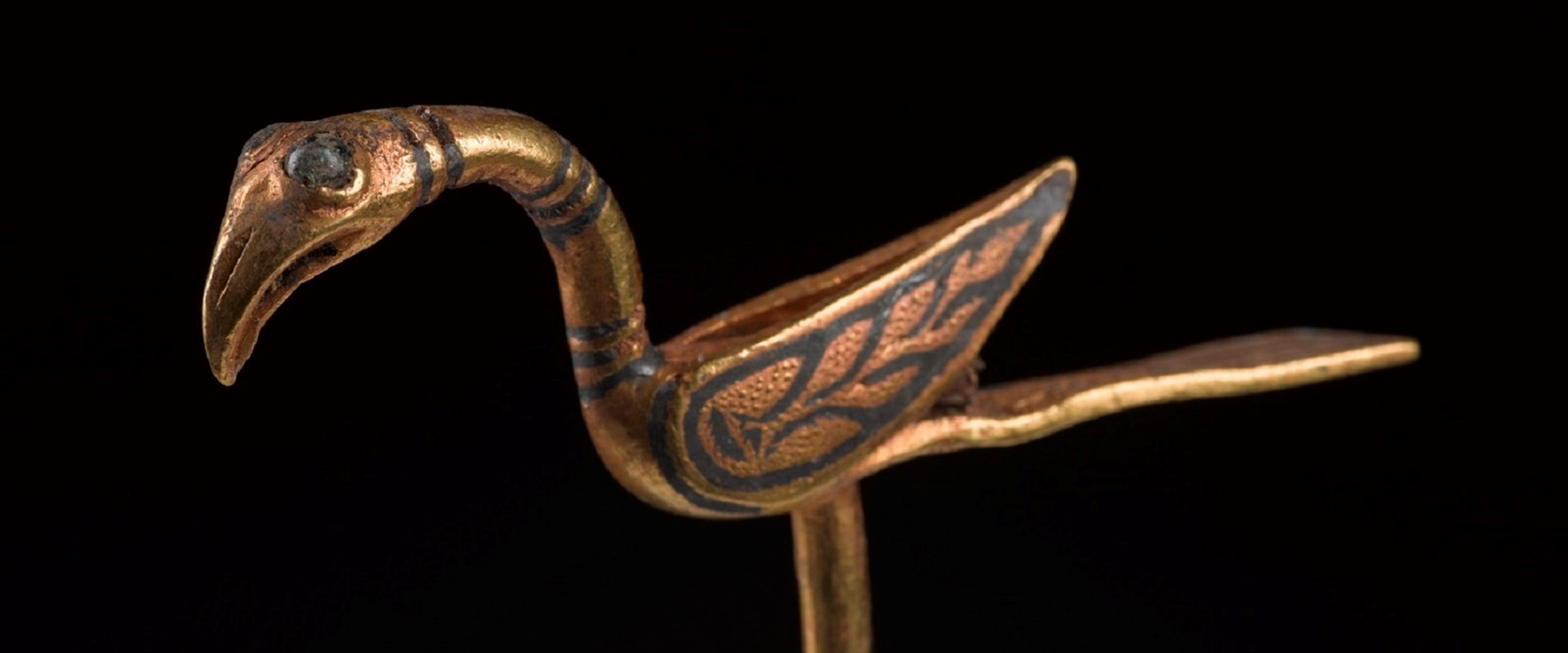Golden pin shaped like a bird, with long, flat tail, upturned wings and flamingo-like beak.