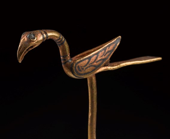 Golden pin shaped like a bird, with long, flat tail, upturned wings and flamingo-like beak.